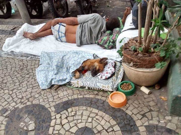 Homeless man improvises bed and blanket for his dog, they are sleeping together on the streets